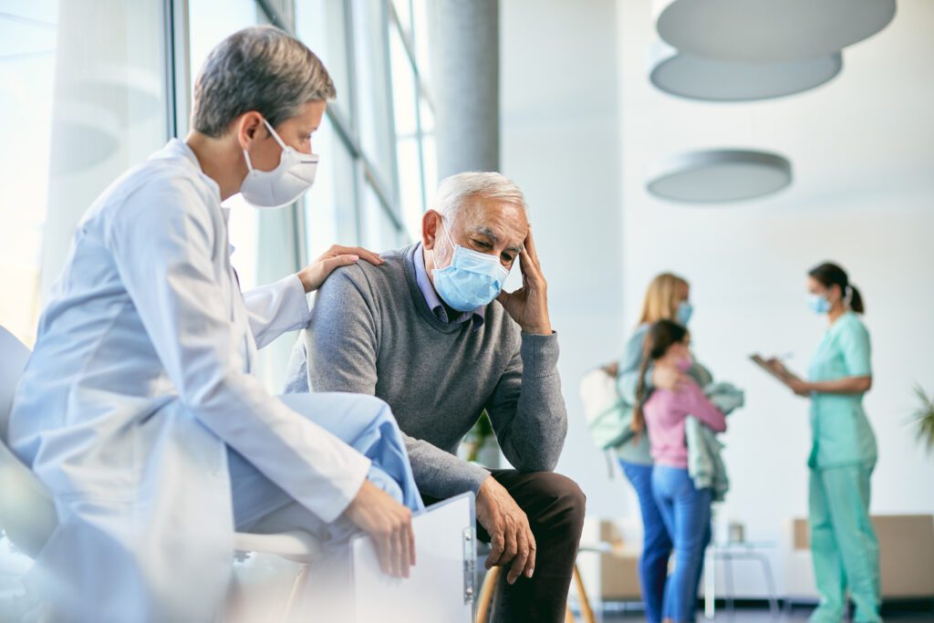 Worried senior man being consoled by female doctor in waiting room at the hospital